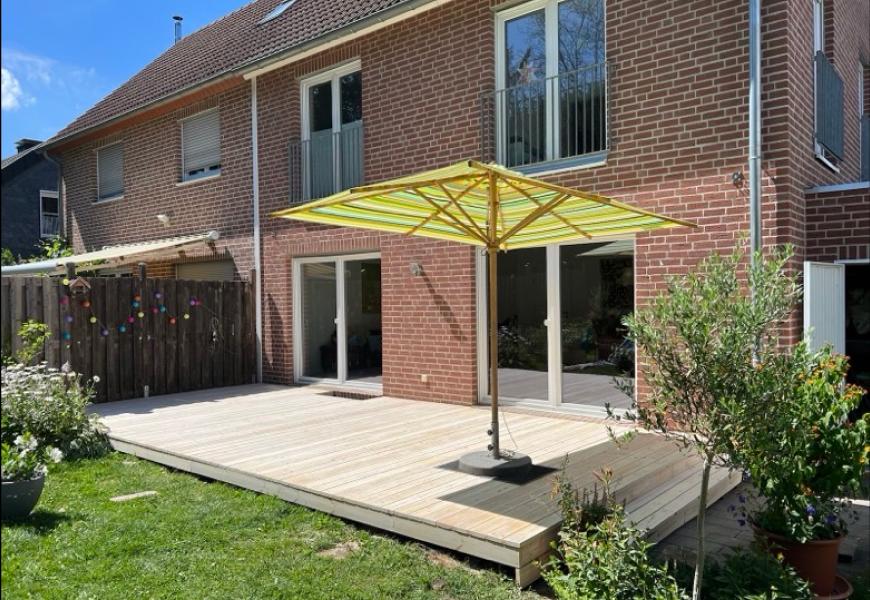 Ein Haus mit einer Terrasse und einem Sonnenschirm im Garten.